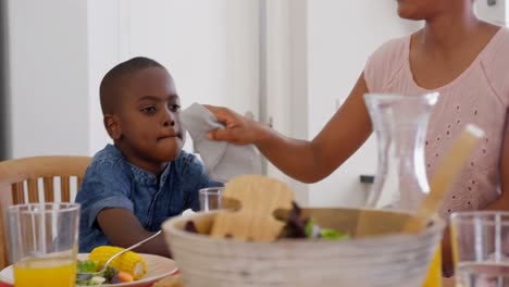 Vista-Frontal-De-Un-Padre-Negro-Adulto-Medio-Limpiando-La-Boca-De-Su-Hijo-En-La-Mesa-Del-Comedor-En-Una-Casa-Cómoda-4k