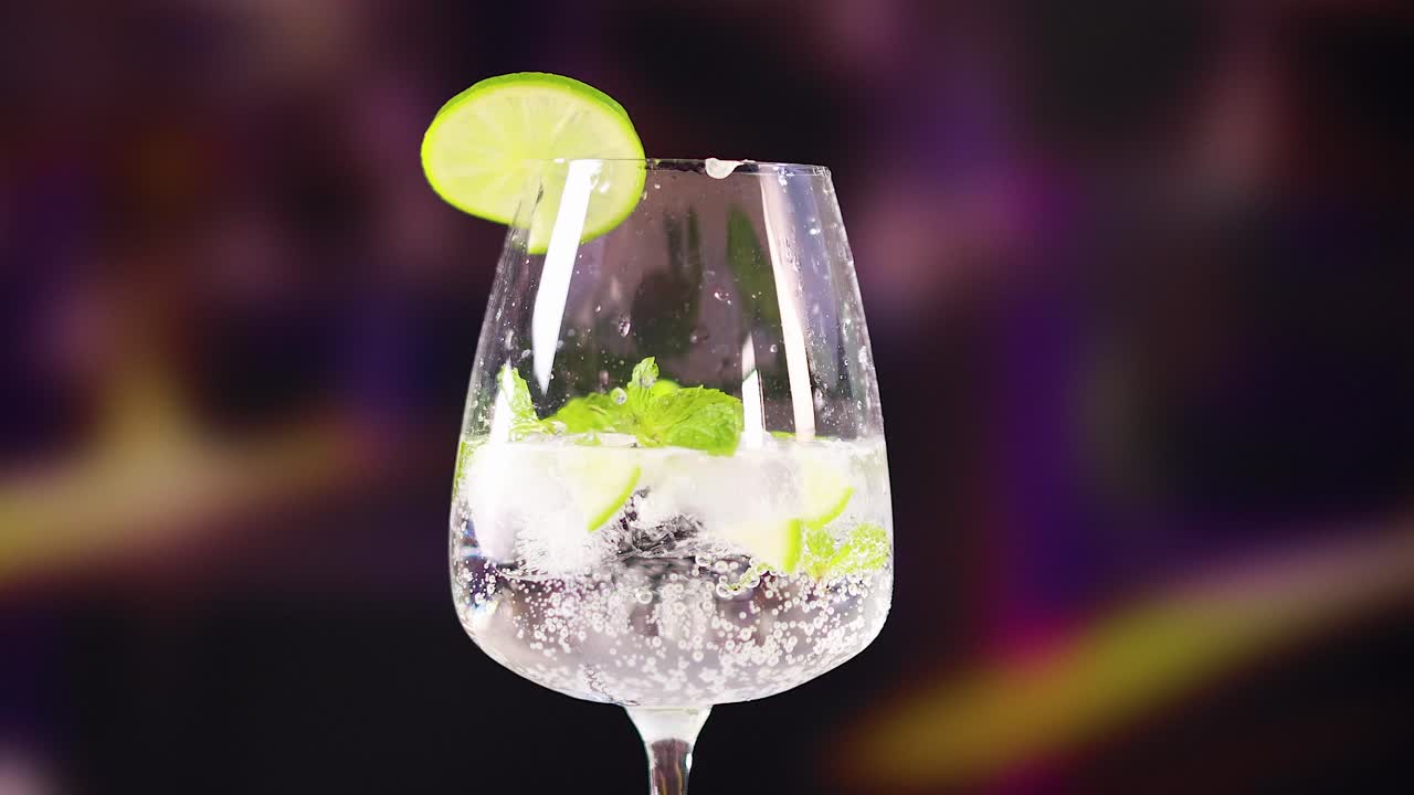 A mojito cocktail is prepared with lime and mint in a lively bar environment, highlighting vibrant colors and dynamic lighting