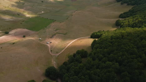 Wohnmobile,-Die-Auf-Dem-Tal-In-Der-Nähe-Von-Dichtem-Wald-In-Der-Toskana,-Italien,-Geparkt-Sind,-Mit-Sonnenlicht,-Das-Von-Wolken-Mit-Schatten-Bedeckt-Ist