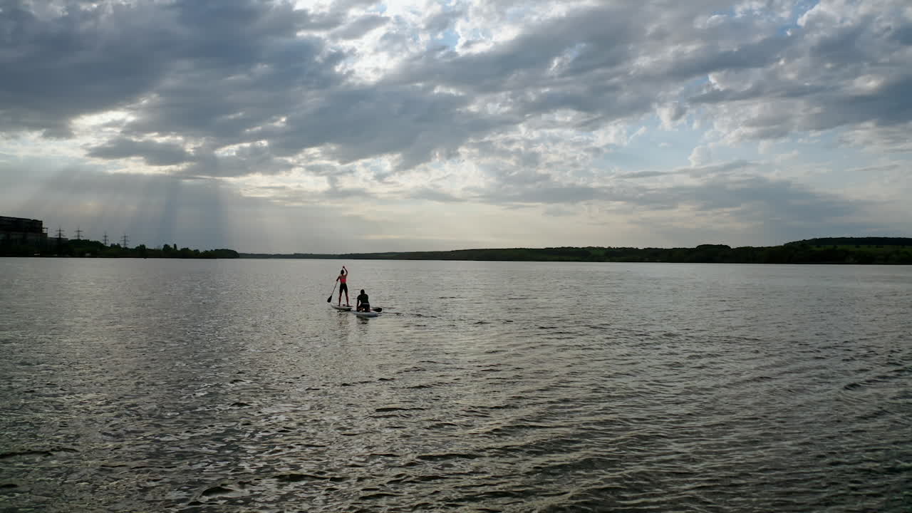 Sailing on boats at dusk. Young people travelling on water on special boards with oars in the middle of a river. Active lifestyle.