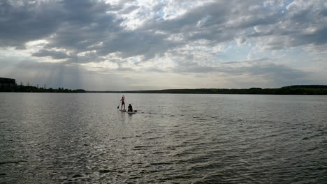 sailing on boats at dusk. young people travelling on water on special boards with oars in the middle of a river. active lifestyle.