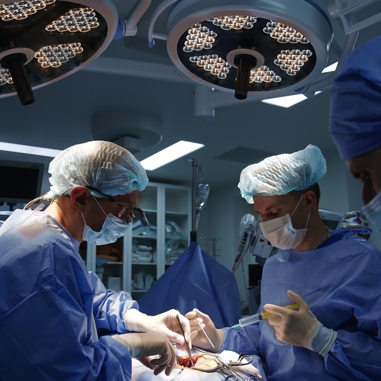 A pair of surgeons bent over the patient applying tools. Two medics are watching the surgery procedure at foreground