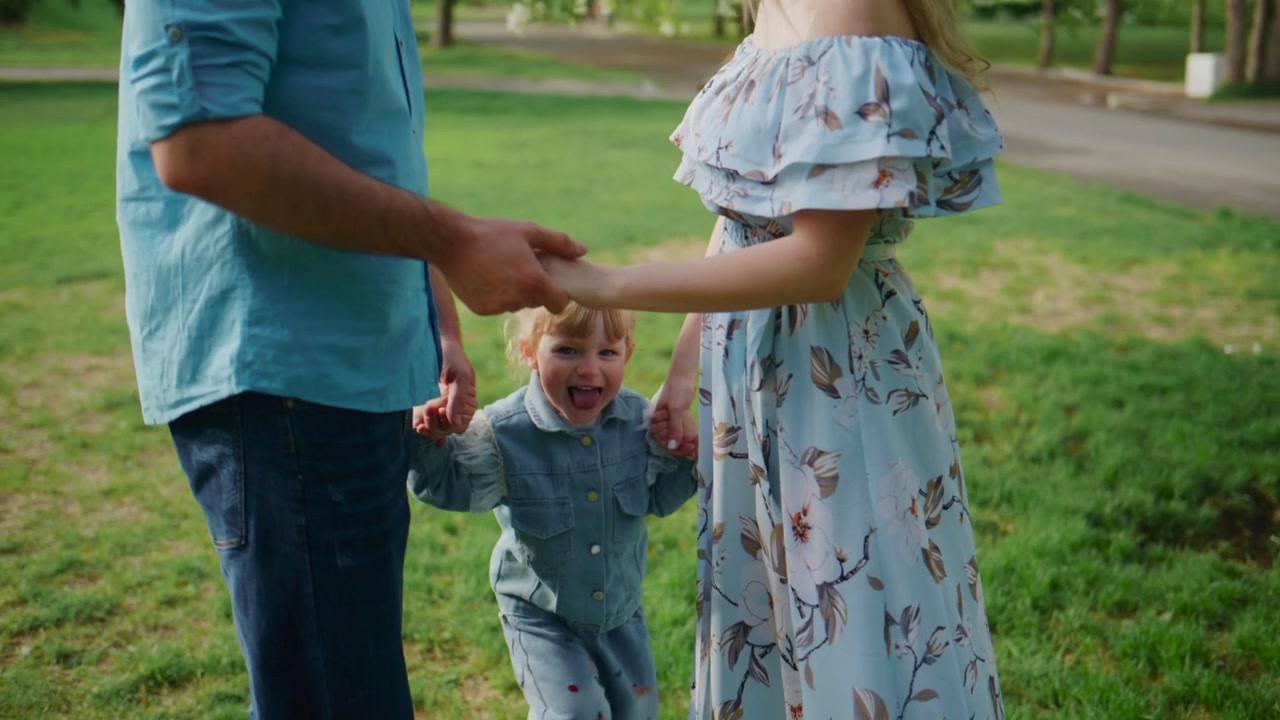Family of three walks hand-in-hand under blooming tree. Mother and father smile, child laughs joyfully. Scene radiates warmth, love, and summer freedom. Ideal for parenting, family