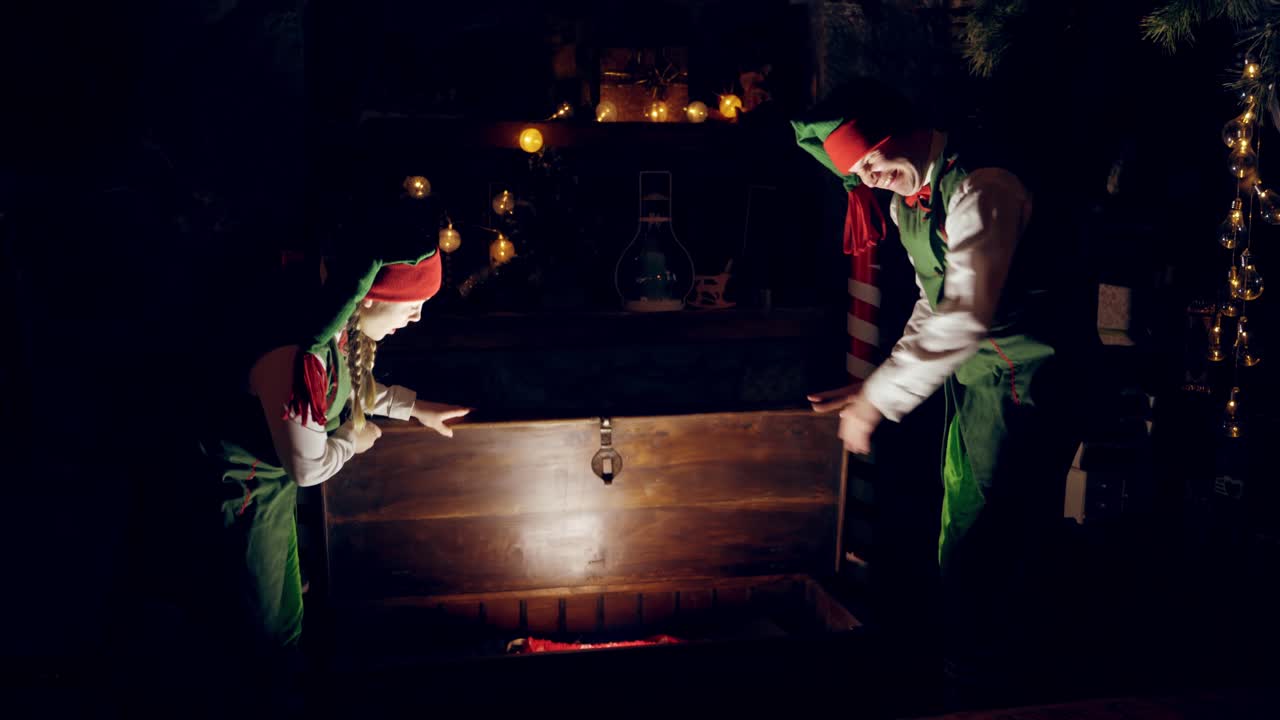 Elves in the dark room at Christmas. Two elves opening glowing coffer and taking a magic red bag for Santa's presents. New Year time.
