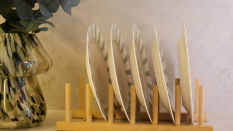 a wooden dish rack holding plates next to a decorative vase