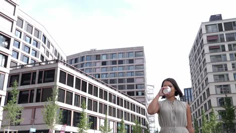 young business woman drinks coffee to go while walking between tall office buildings in financial district during her break