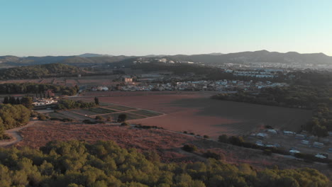 drone flying over treetops, farmland towards farmed fields with panoramic views of city mountains far away at horizon