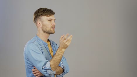 waist up three quarter angle studio shot of pensive young man thinking with his hand on chin and expressing his opinion for somebody standing against grey background, copy space to right