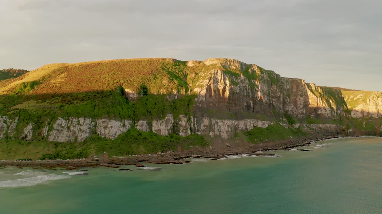 뉴질랜드의 해안선을 따라 산맥을 치는 태양 광선으로 일몰 동안 궤도를 도는 샷