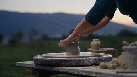 hands shaping clay on a potter's wheel at sunset