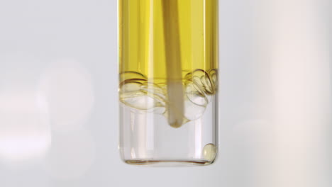 A-container-of-yellow-oily-liquid-being-stirred-with-a-bright-white-background