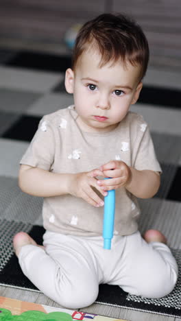 caucasian baby focused on the camera. kid sits on the floor holding and turning the toy in his hands. vertical video