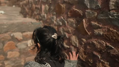 Woman-exploring-old-stone-ruins-on-a-sunny-day,-close-up-of-hand-touching-the-stones,-over-the-shoulder-shot