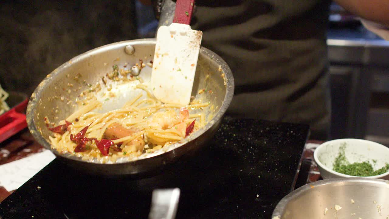 En professionel kok i sorte handsker kaster spaghettipasta på en pande over høj varme