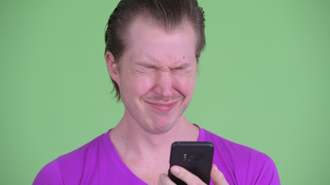 zoom en la toma de un joven que parece sorprendido y conmocionado mientras usa el teléfono móvil contra un fondo verde