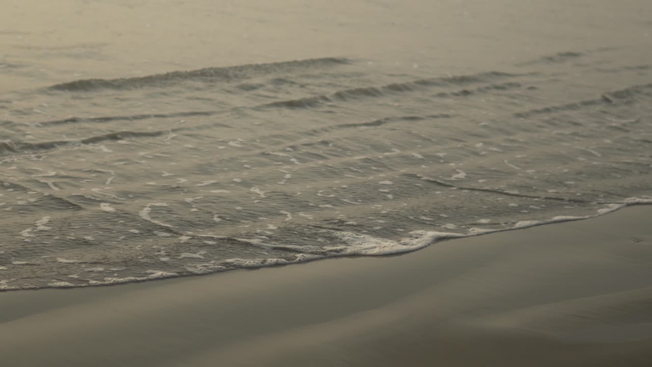 부드러운 물결은 가게 해가 지는 부드러운 황금빛 하늘 아래 모래 해변을 는다.