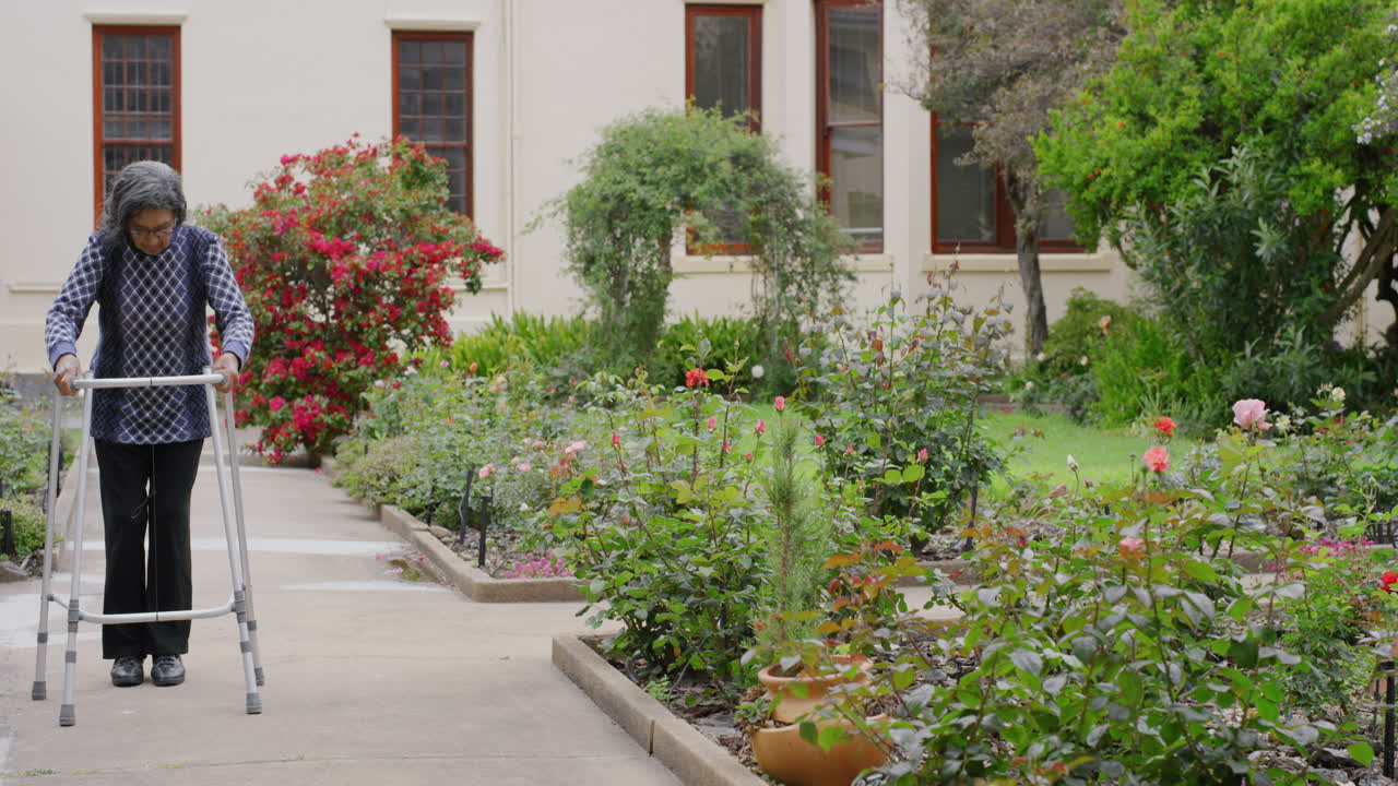 보행기를 사용하는 노인 인도 여성 아름다운 정원 길을 천천히  ⁇ 고 평화로운 산책을 즐기며 평온한 은퇴 생활 방식을 즐기고 있습니다.