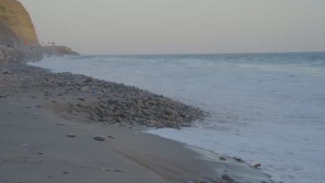 Schwenk-Vom-Pacific-Coast-Highway-Zum-Pazifischen-Ozean,-Während-Die-Wellen-Am-Strand-Von-Mondo-In-Der-Abenddämmerung-In-Südkalifornien-Auf-Die-Küste-Treffen