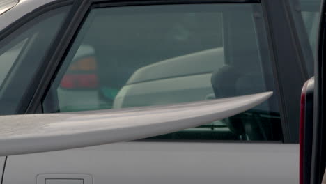 person carefully taking out surfboard from car trunk in static view