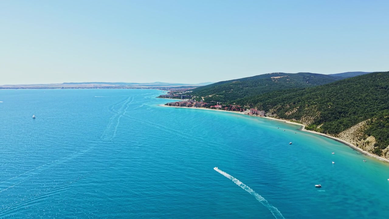 Güneşli bir günde, küçük bir kasabanın yakınında, uzakta su ve karanın görüldüğü net bir kıyı manzarası.