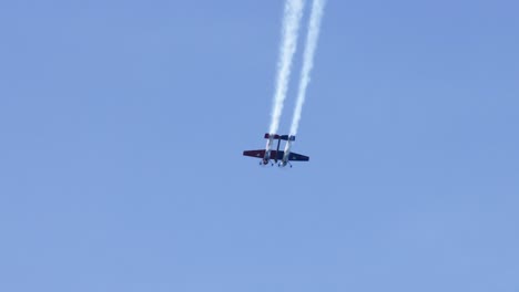 biplane executes maneuvers with smoke trails in sky