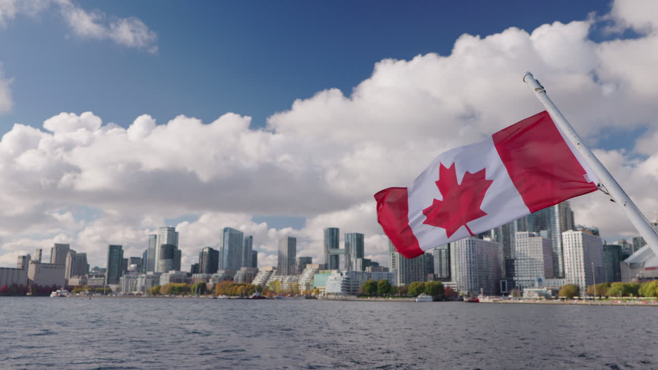 Bandiera canadese che sventola su una barca con lo skyline di Toronto sullo sfondo, paesaggio urbano sul lungomare del Lago Ontario con edifici moderni sotto nuvole drammatiche.