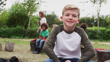 Porträt-Eines-Jungen-Auf-Einem-Outdoor-Campingausflug,-Der-Mit-Freunden-Am-Lagerfeuer-Sitzt