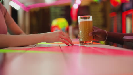 barman gives beer to woman client at counter closeup. lady guest orders craft lager from black barkeeper in night club. customer rests in stylish pub