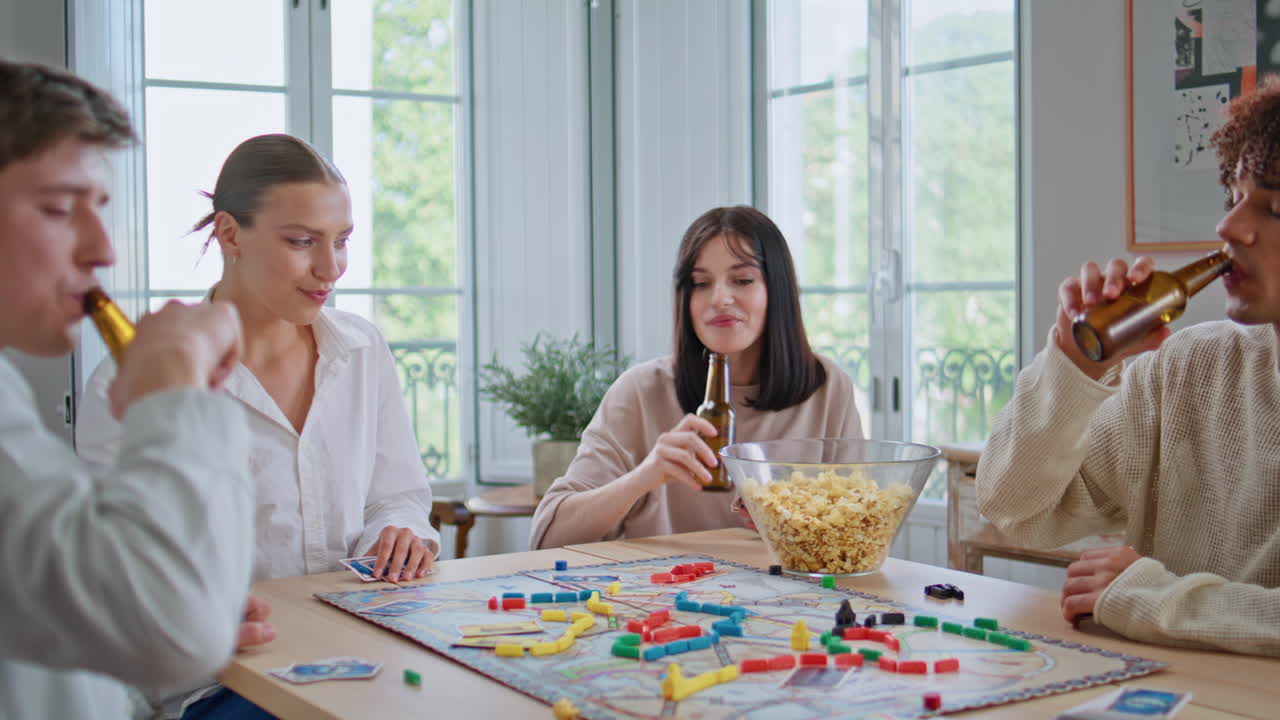 Happy youngsters toasting beer play board game kitchen closeup. Diverse friends