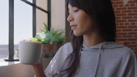 beautiful young asian woman drinking coffee at home enjoying relaxed morning looking out window smiling happy in trendy apartment