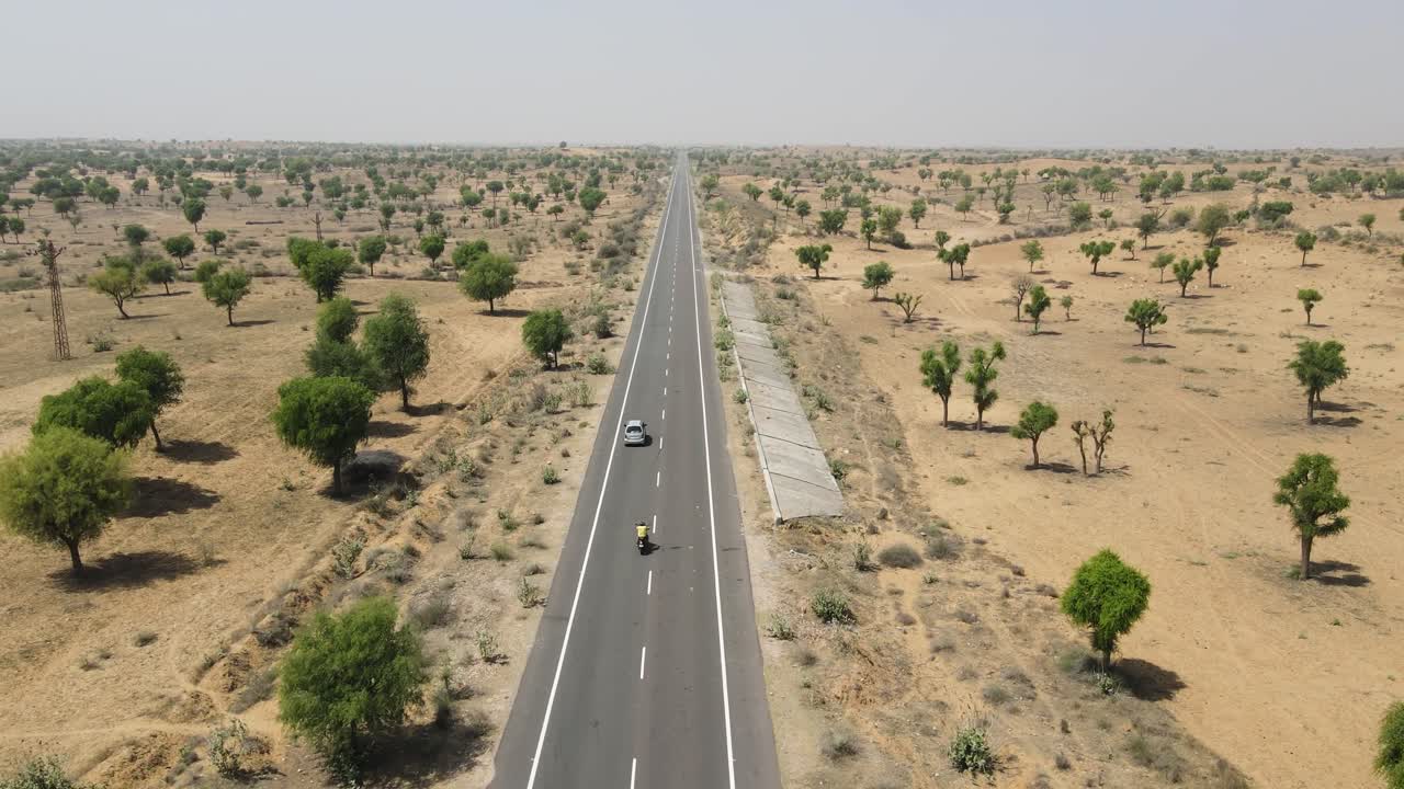 Aerial drone shot showcasing a car driving through the arid desert landscape of Rajasthan under clear skies.