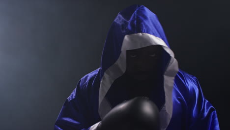 Portrait-Of-Boxer-Wearing-Robe-Entering-Ring-At-Start-Of-Boxing-Match-Hitting-Gloves-Together-With-Low-Key-Lighting-2