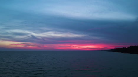 Red-pink-vibrant-light-glows-below-dark-blue-grey-clouds-along-the-coastal-waters