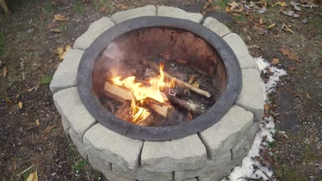 Wide-top-view-of-fire-burning-in-a-fire-pit-with-snow-and-leafs-on-the-ground