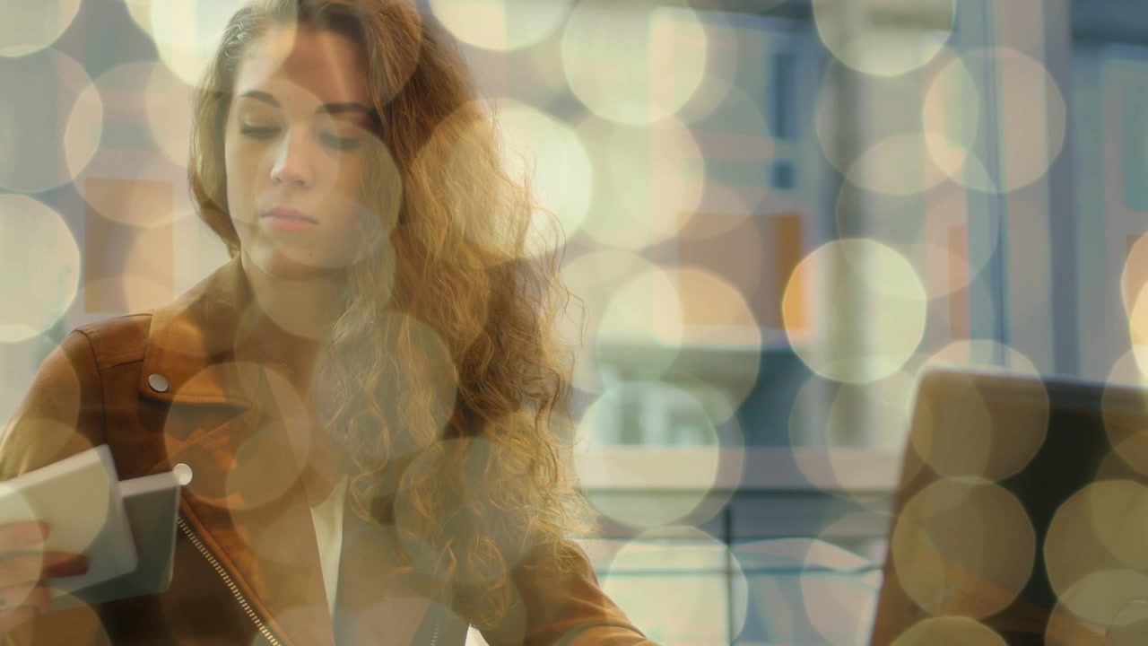 Woman picking up card checking planner taking notes while glancing laptop bokeh overlaying for work