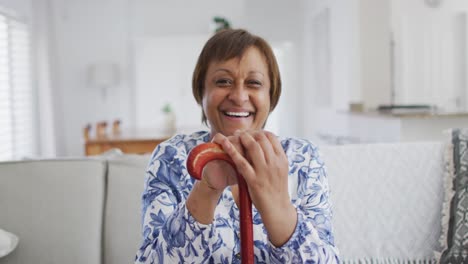 Portrait-of-happy-african-american-senior-woman-sitting-leaning-on-walking-stick,-smiling