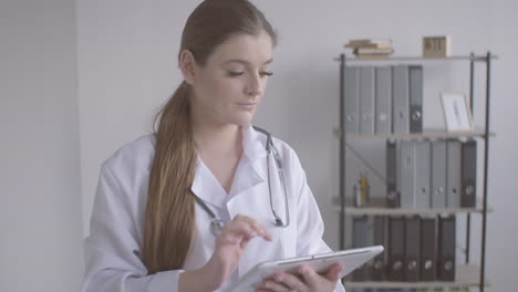 doctora pelirroja con bata blanca usando una tableta y mirando la cámara 1