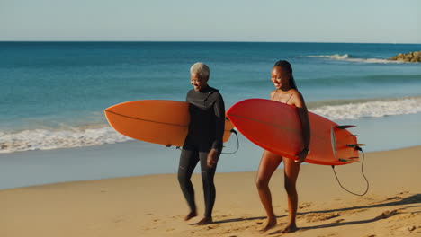 two women walking on the beach with their surfboards