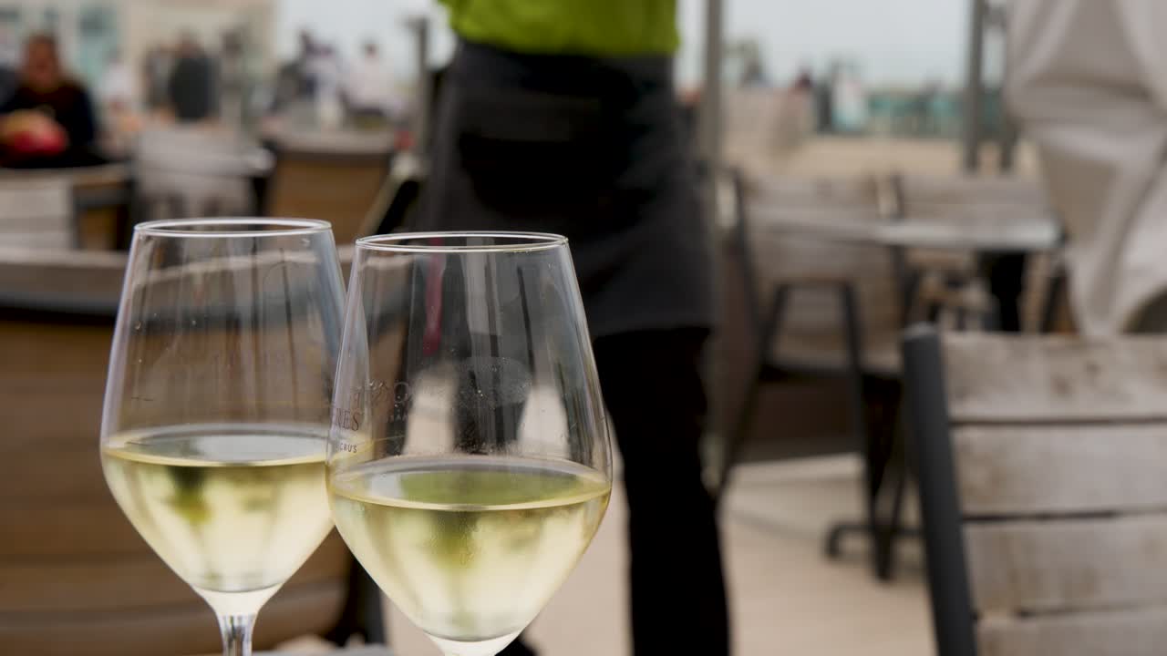 Two white wine glasses on outdoor seaside cafe table, shallow focus, natural daylight, relaxed mood
