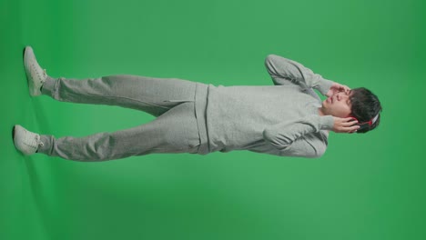 full body of side view asian man listening to music with headphones and dancing in the green screen studio