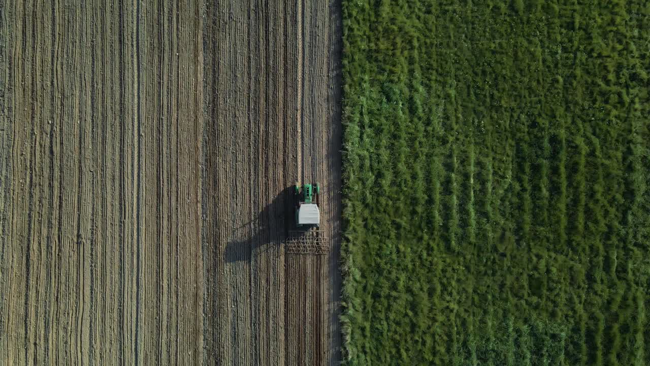 toma aérea de un tractor arando un campo agrícola junto a un campo de hierba verde a la luz del sol