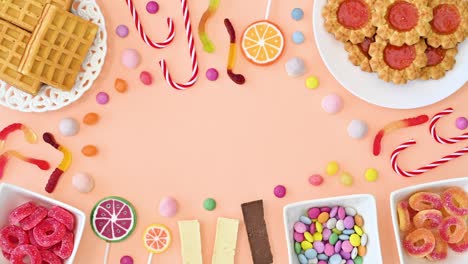 creative frame copy space with sweet cookies, candies and lollipops on pastel bright orange backgorund. stop motion flat lay