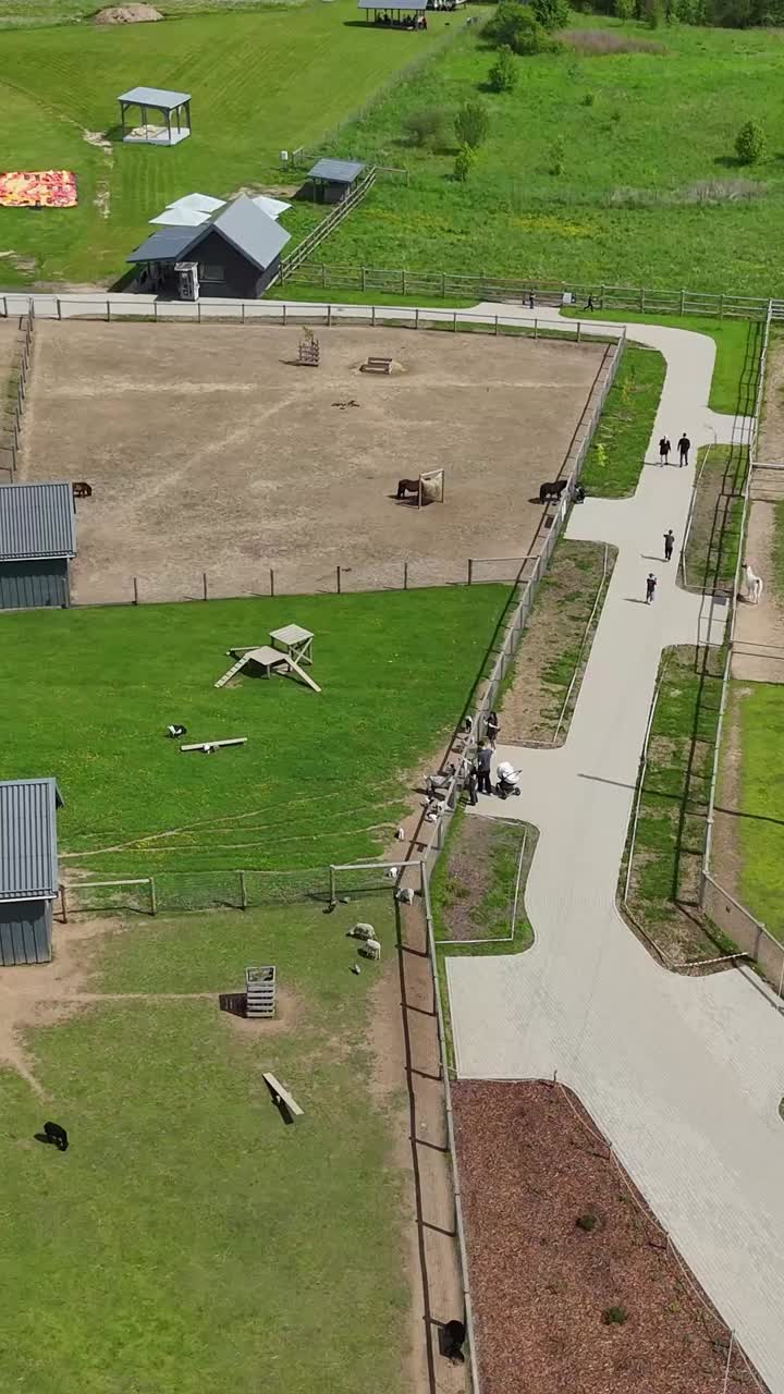 Vertical drone shot over little Zoo shows goats and birds in pens with feeding structures, alongside walking paths and small barns in the countryside zoo