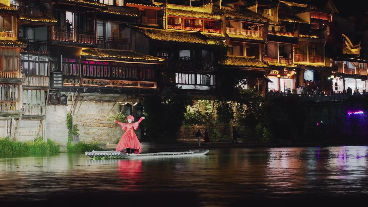Caminhada noturna junto ao rio com edifícios iluminados, artista feminina de vestido vermelho desliza por uma plataforma de madeira perto da margem, arquitetura tradicional iluminada por lanternas, reflexos cintilam na água calma.
