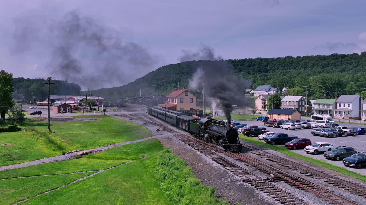 A classic steam train departs from a quaint town, moving along picturesque tracks surrounded by lush greenery and rolling hills.