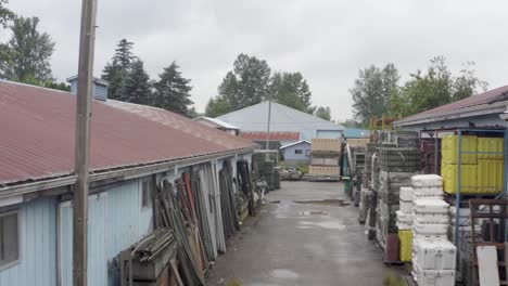 military storage alley of vintage parts on a rainy wet day aerial through an alley of vintage ww2 building with a gradual rise.