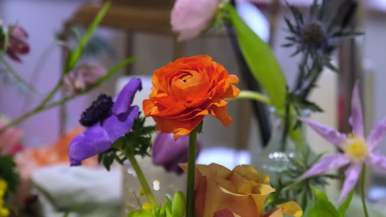 Orange Rose and a Purple Anemone displayed with many other flowers at wedding event.