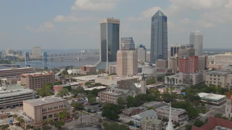 an aerial pull back shot with the jacksonville downtown skyline and city surrounded by water on a mildly overcast day