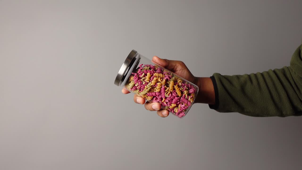 Hand holding a jar of colorful pasta