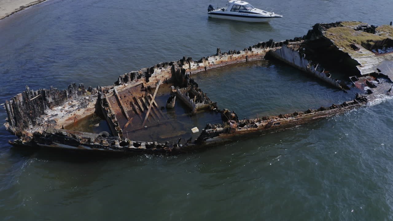 Ships graveyard.A derelict partially submerged shipwreck aground near the shore in the afternoon. Aerial pivot  shot.